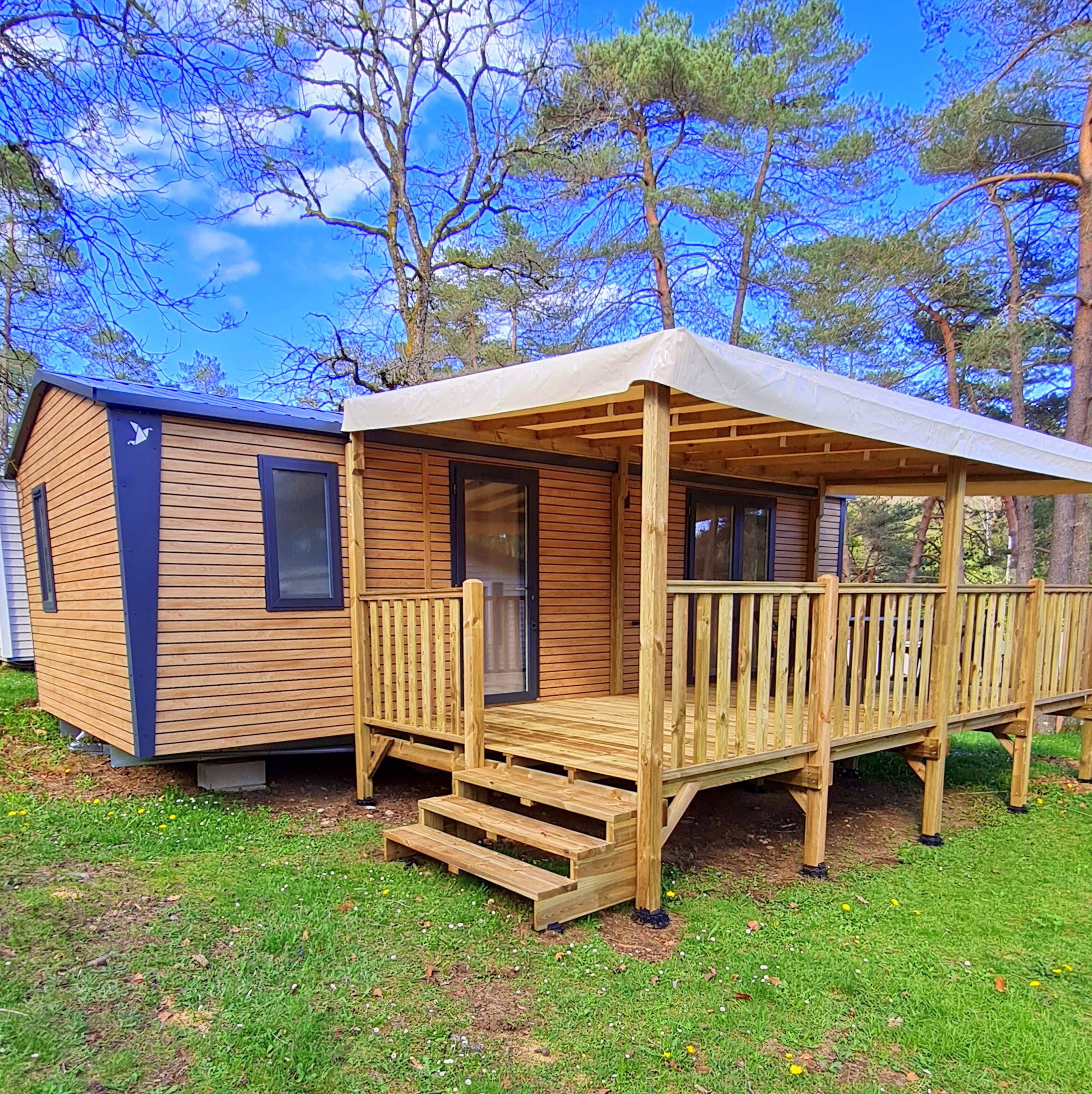 Mobil-home supérieur glamping 2 chambres tout équipé avec terrasse, parasol et salon de jardin au camping Les Trois Sources, hébergement familial et animaux acceptés.