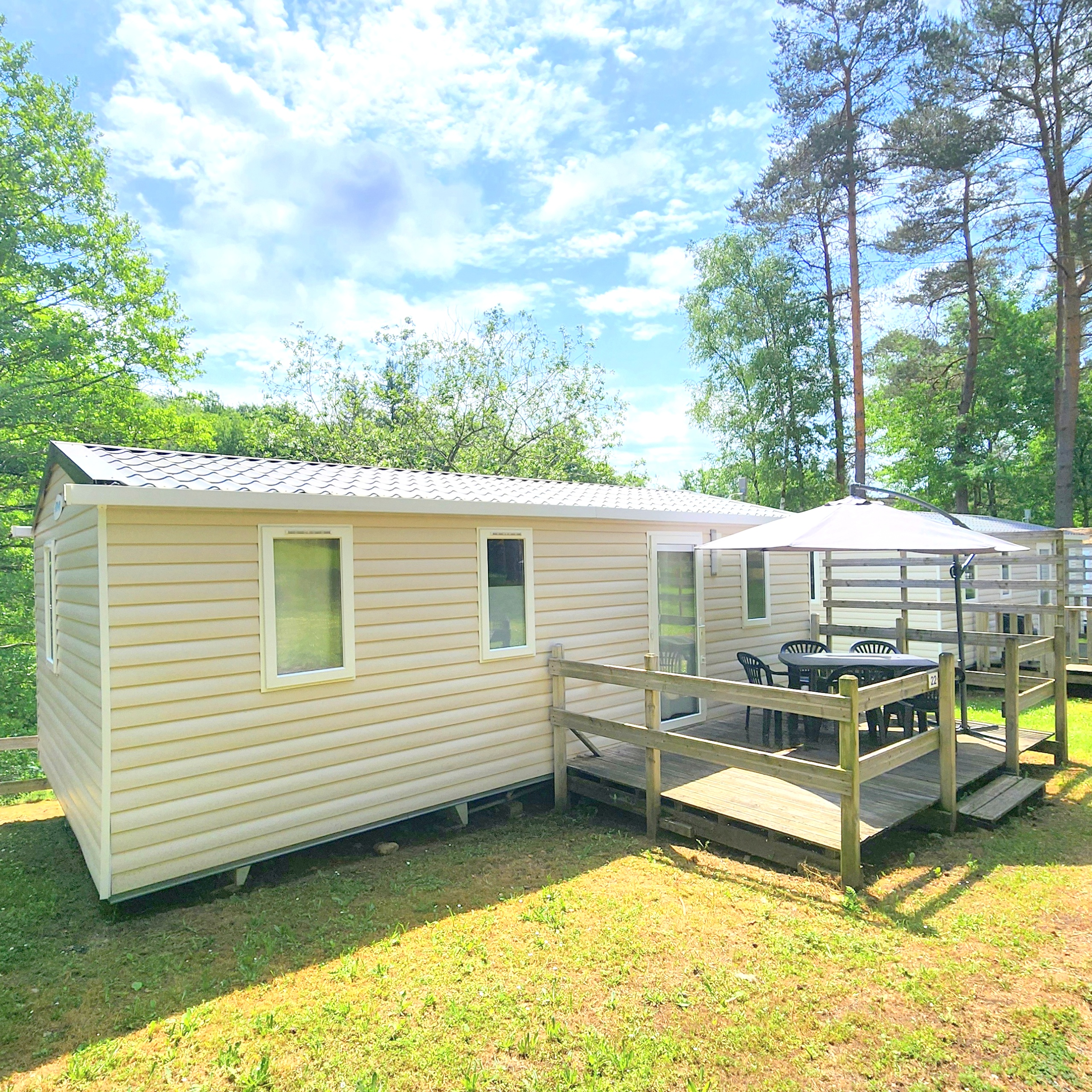 Mobil-home Confort 2 chambres tout équipé avec terrasse, parasol et salon de jardin au camping Les Trois Sources, hébergement familial et animaux acceptés.