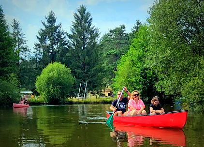 Famille de trois personnes en canoë rouge sur l'étang du camping Les Trois Sources, moment nature et détente en famille.